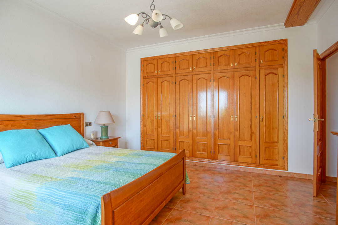 Dormitorio con amplio armario empotrado de madera maciza hecho a medida, suelo de gres cerámico y mobiliario de madera a juego.