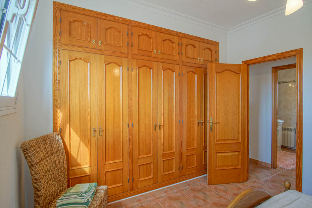 Dormitorio con amplios armarios empotrados de madera maciza hechos a medida, suelos de gres y acceso directo a un baño privado.