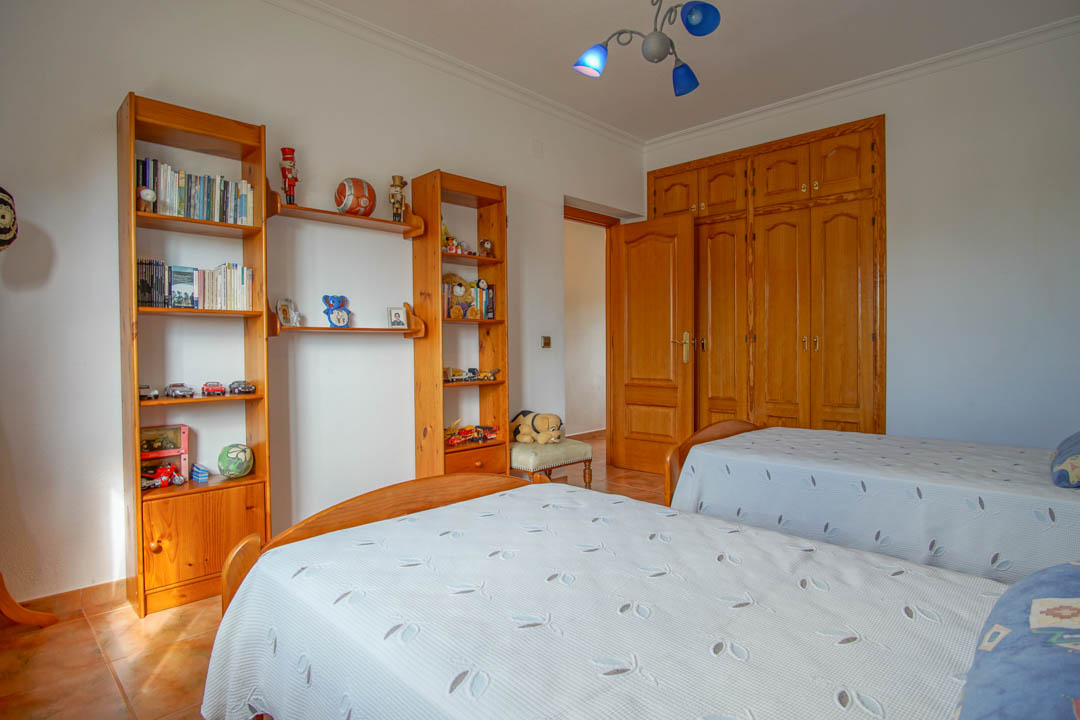 Dormitorio con dos camas individuales, armarios empotrados de madera maciza a medida y estanterías coordinadas sobre suelo de gres cerámico.