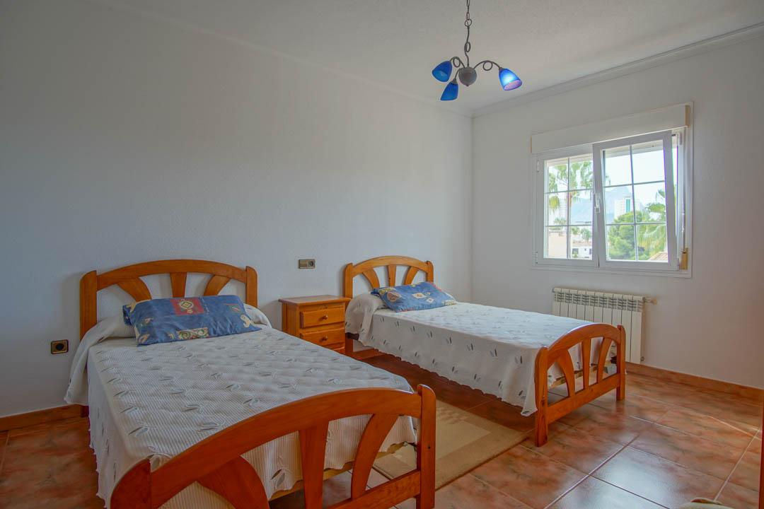 Dormitorio con dos camas individuales de madera maciza, suelos de gres y ventana con vistas exteriores que aporta abundante luz natural.