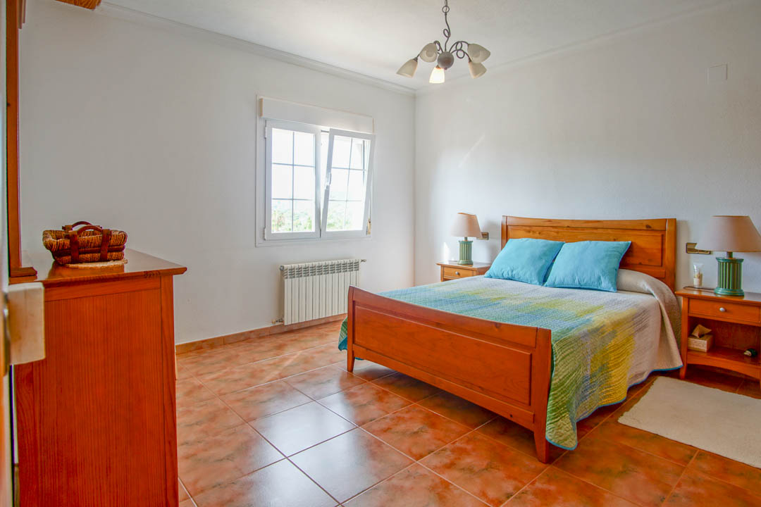 Dormitorio con mobiliario de madera maciza, suelos cerámicos de tono terracota y ventana de doble acristalamiento que aporta luz natural.