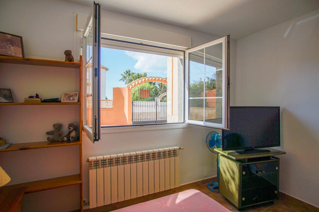 Dormitorio con ventana de doble hoja abierta, radiador de calefacción y estantería de madera maciza, con vistas despejadas al acceso exterior de la propiedad.
