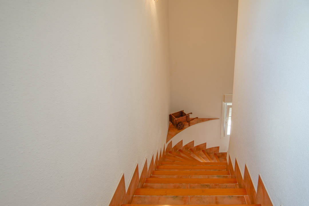Escalera interior con peldaños de gres cerámico y rodapié a juego, paredes blancas texturizadas y un detalle decorativo de madera en el rellano.