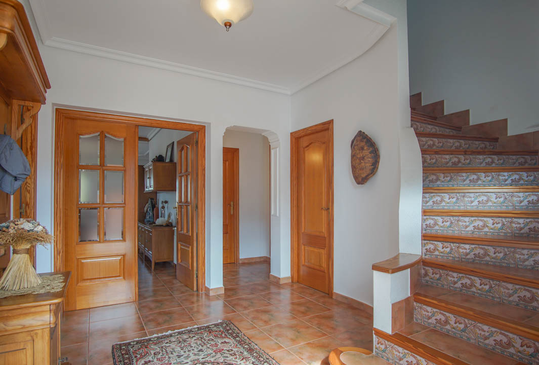Hall de entrada con suelos cerámicos, carpintería de madera maciza y una escalera con contrahuellas decoradas con azulejos tradicionales.