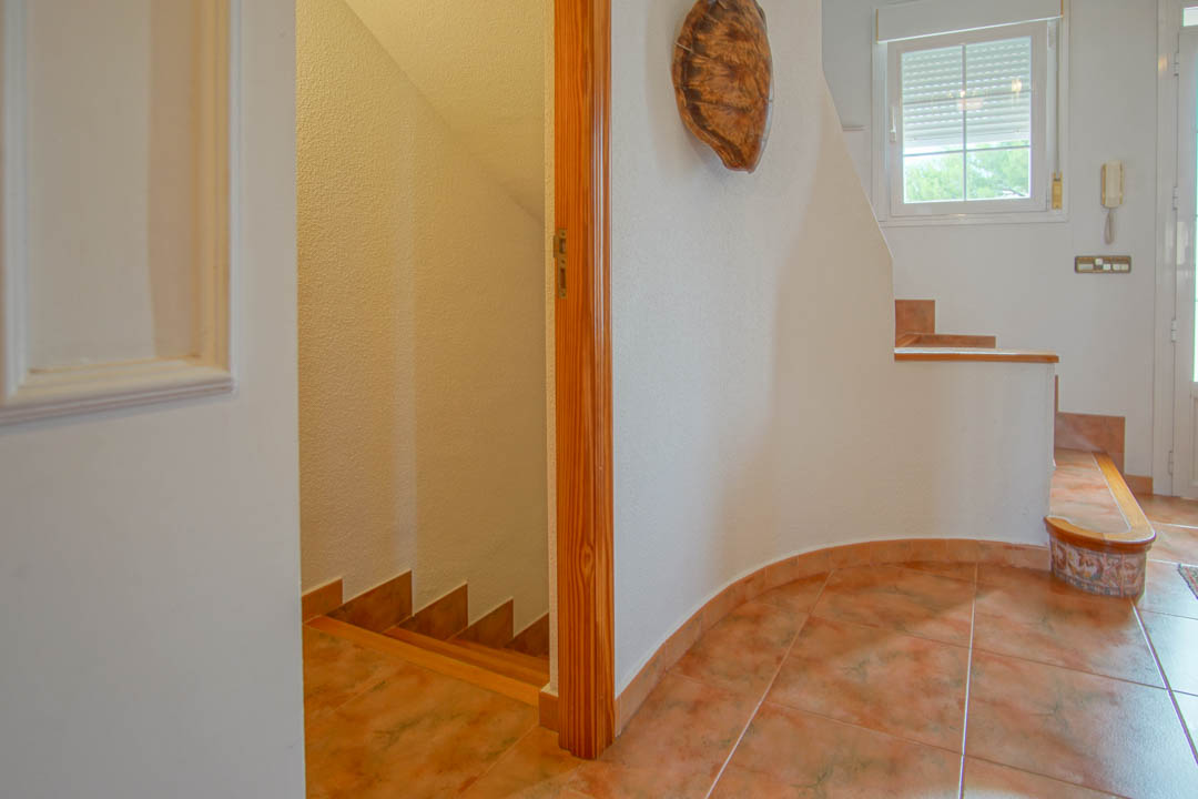 Hall de entrada con suelos cerámicos y carpintería de madera maciza, mostrando el acceso a las escaleras que conectan los tres niveles de la vivienda.