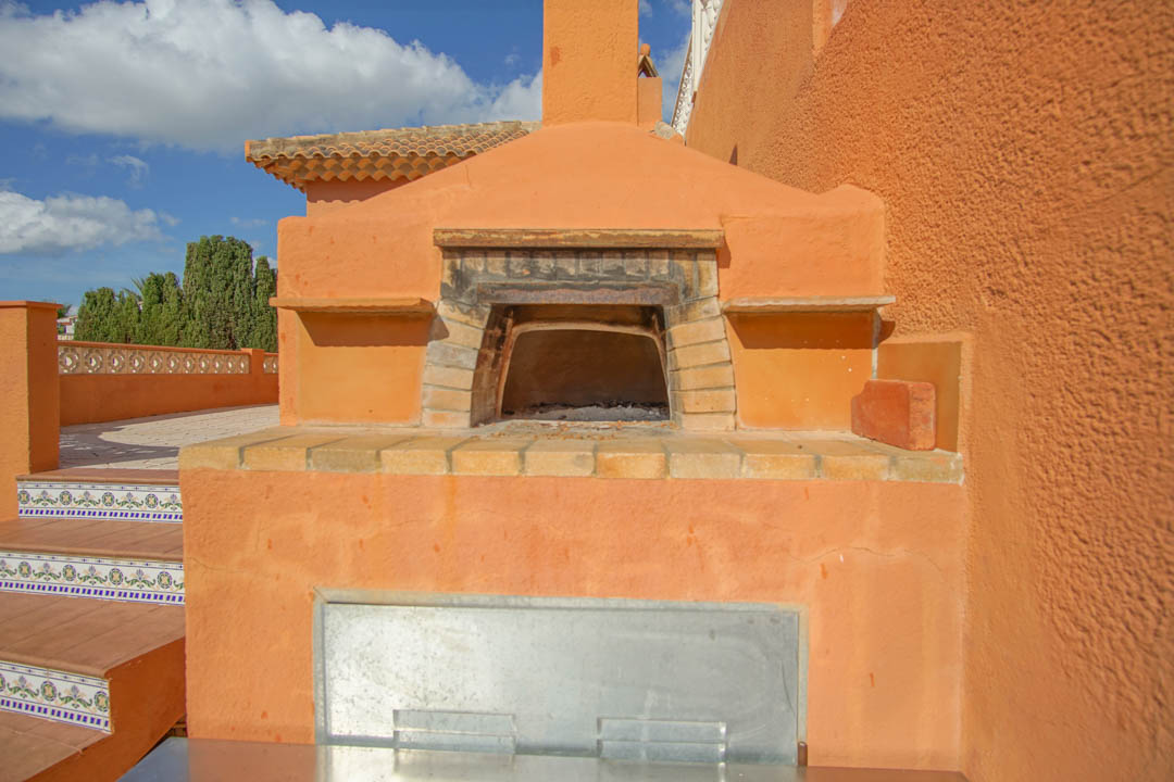 Horno de leña tradicional integrado en la zona exterior, con arco de ladrillo y chimenea sobre una estructura de color terracota junto a escaleras decoradas.