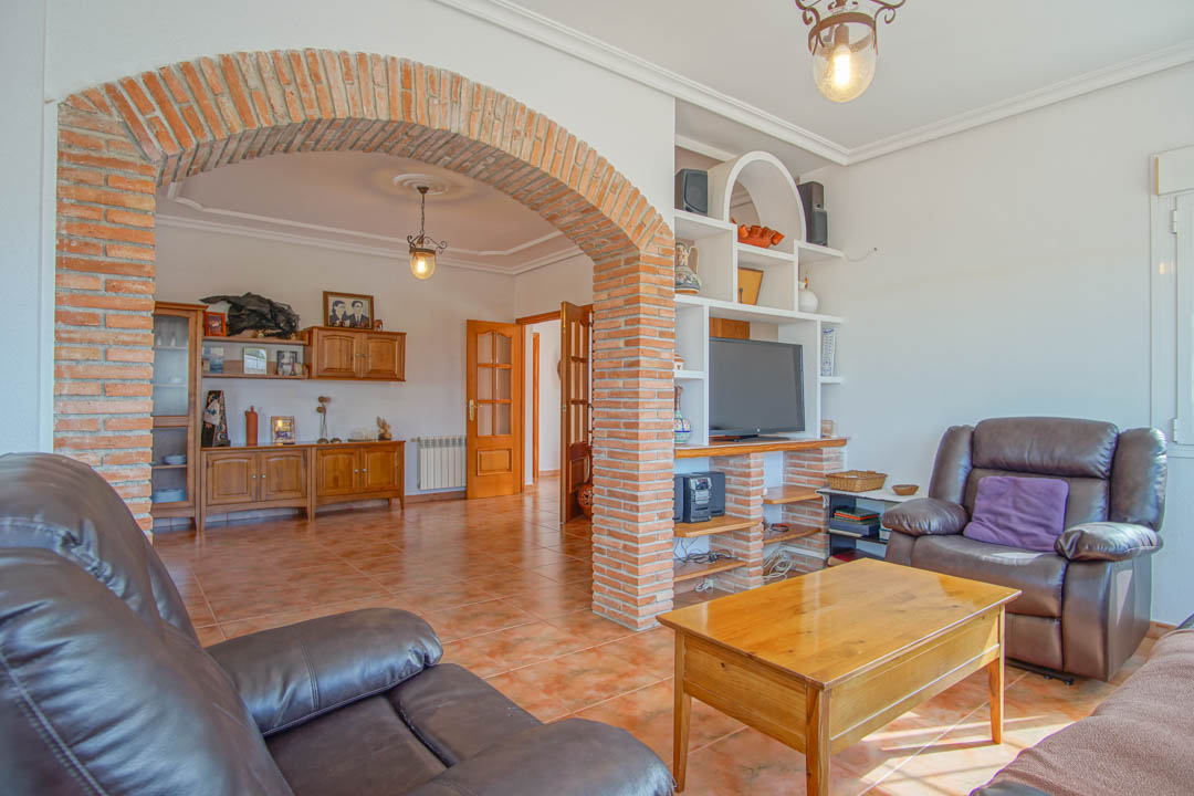 Salón con un arco de ladrillo visto que separa los ambientes, suelos de gres rústico y mobiliario de madera maciza con estantería de obra integrada para la televisión.