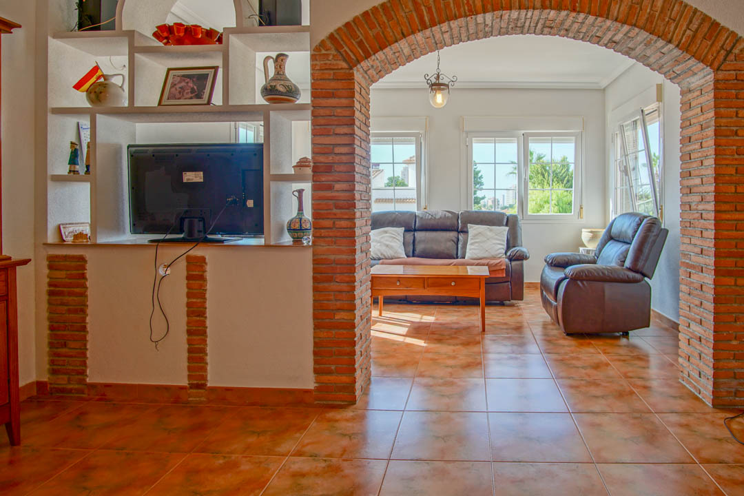 Salón rústico con arco de ladrillo visto, suelos de gres cerámico y zona de estar luminosa con sofás de cuero y ventanales al exterior.