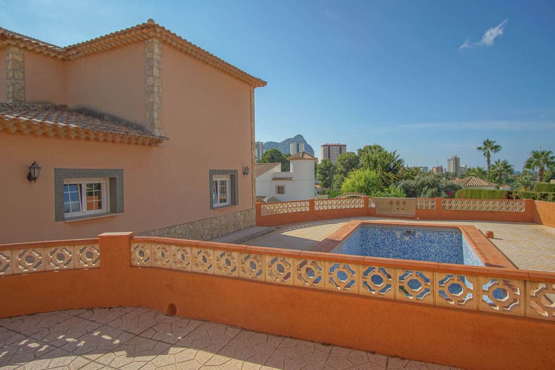 Vista exterior de la villa con piscina privada y terraza pavimentada, destacando las vistas despejadas hacia el Peñón de Ifach y el entorno urbano.