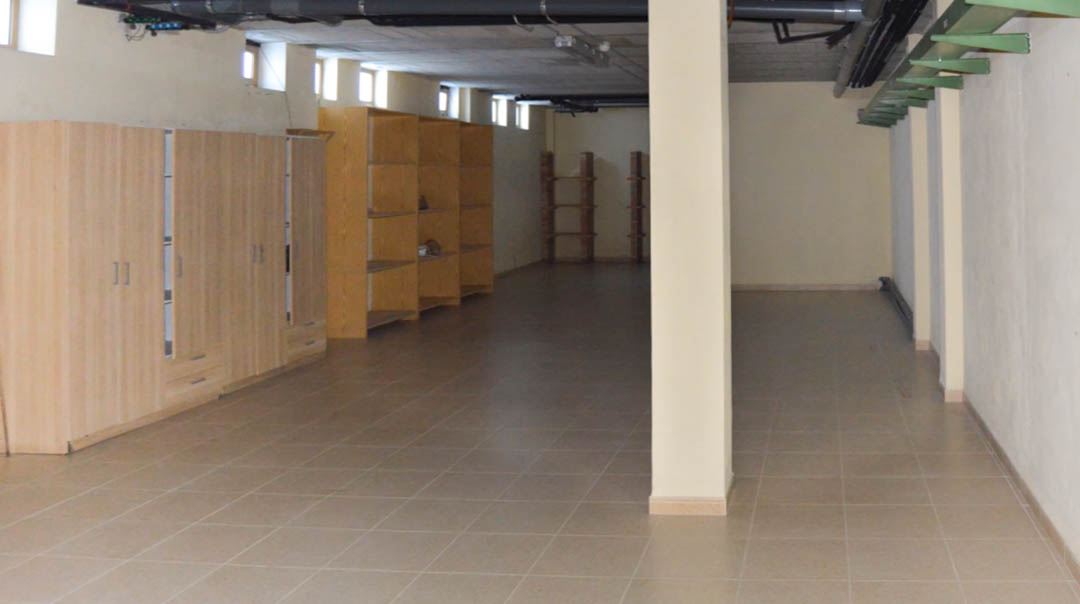 Amplio espacio técnico subterráneo con suelos cerámicos, columnas de soporte y armarios de madera. Incluye instalaciones a la vista y pequeñas ventanas superiores.