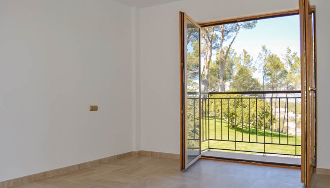 Dormitorio luminoso con suelos de gres y puertas de madera de alta calidad que dan acceso a un balcón privado con vistas a los jardines y la pinède circundante.
