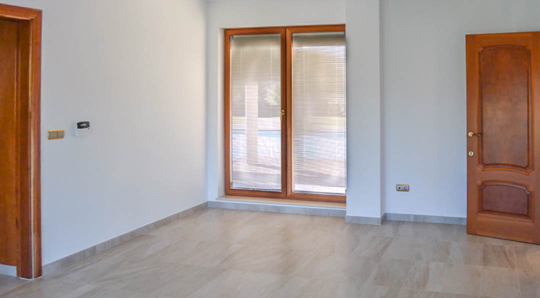 Habitación luminosa con suelos de piedra natural, carpintería de madera maciza de alta calidad y grandes ventanales con persianas integradas hacia el exterior.
