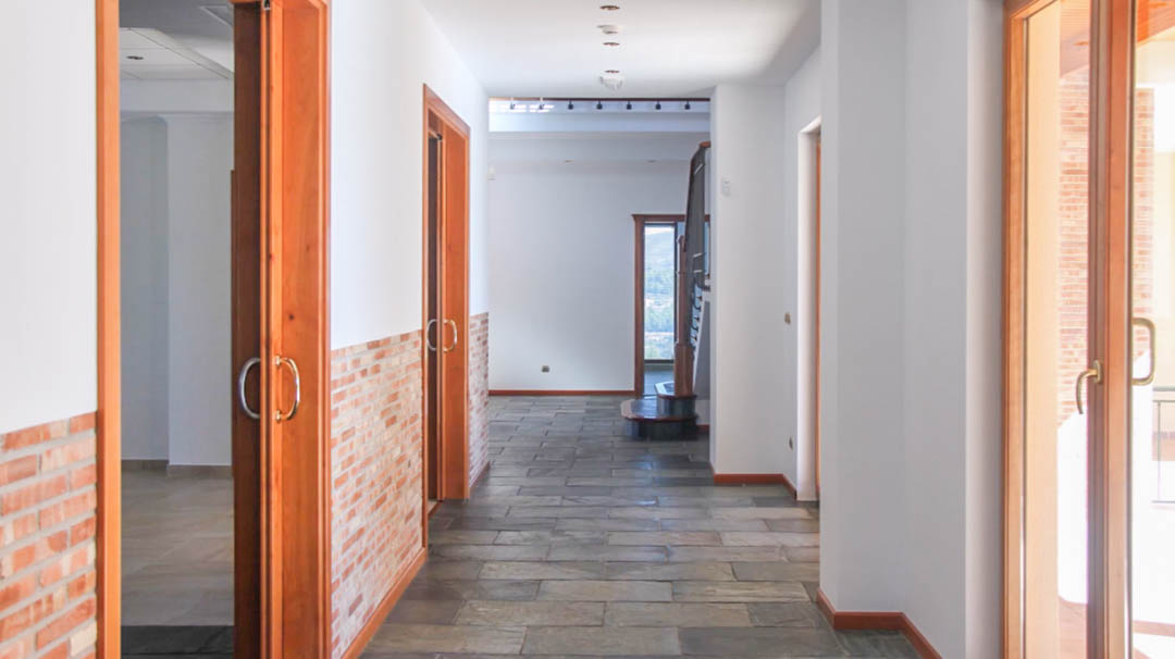 Pasillo con suelos de piedra natural, zócalos de ladrillo visto y puertas correderas de madera de alta calidad que dan paso a las estancias principales.