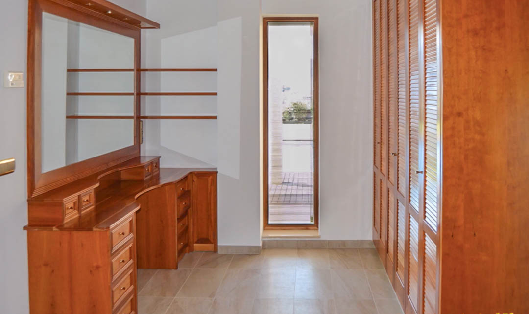 Vestidor con armarios de madera de alta calidad, tocador integrado con espejo y luz natural a través de un ventanal vertical.