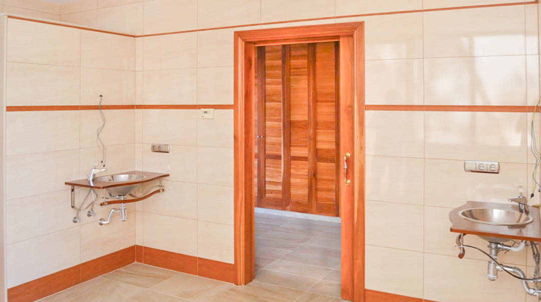 Zona de aseo con lavabos de acero inoxidable y paredes alicatadas, con acceso a un vestidor con armarios de madera de alta calidad.