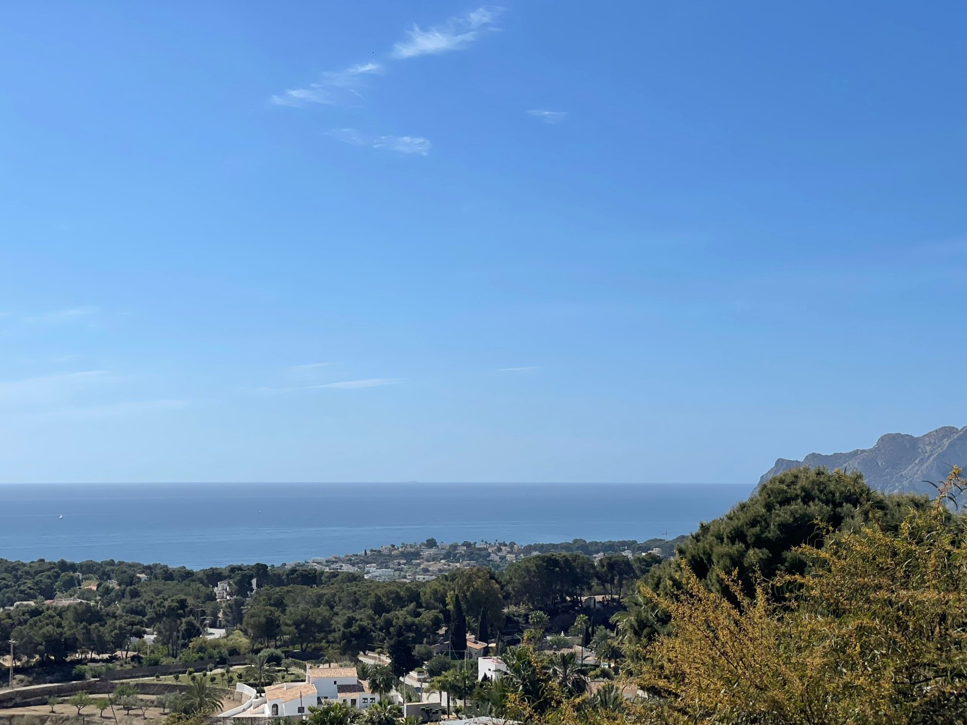 Vista panorámica de la costa de Benissa, mostrando la vegetación mediterránea, villas residenciales y el mar bajo un cielo despejado.