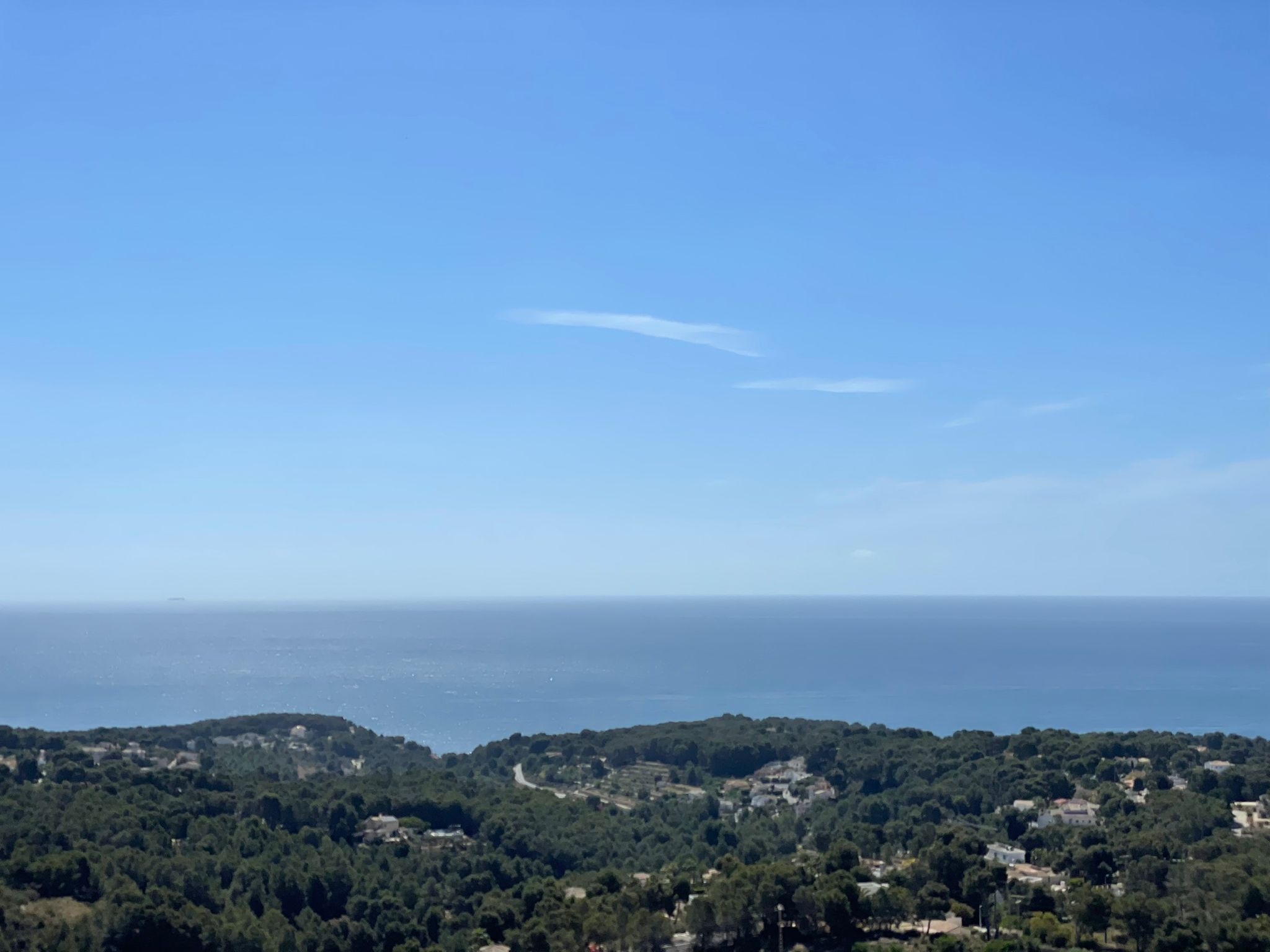 Vista panorámica del mar Mediterráneo y la costa arbolada de Benissa bajo un cielo despejado, destacando la elevación y el entorno natural de la zona.