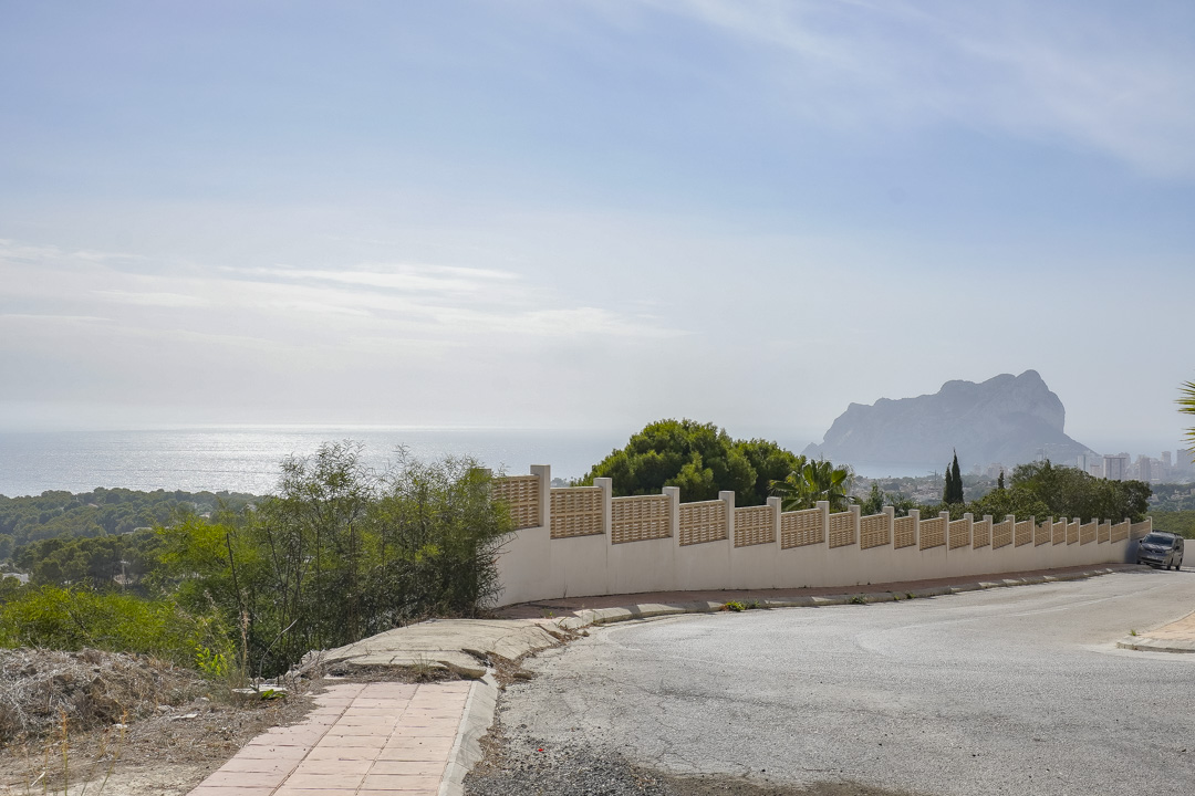 Vista panorámica desde la calle de acceso, mostrando el muro perimetral de la propiedad y el Peñón de Ifach sobre el mar Mediterráneo.