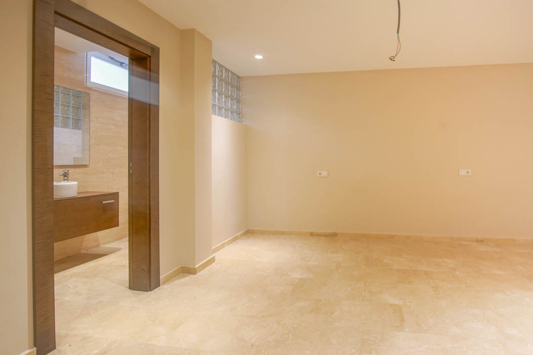 Dormitorio con suelos de piedra natural y baño en suite. Incluye un mueble de lavabo suspendido en madera y detalles de bloques de vidrio para luz natural.