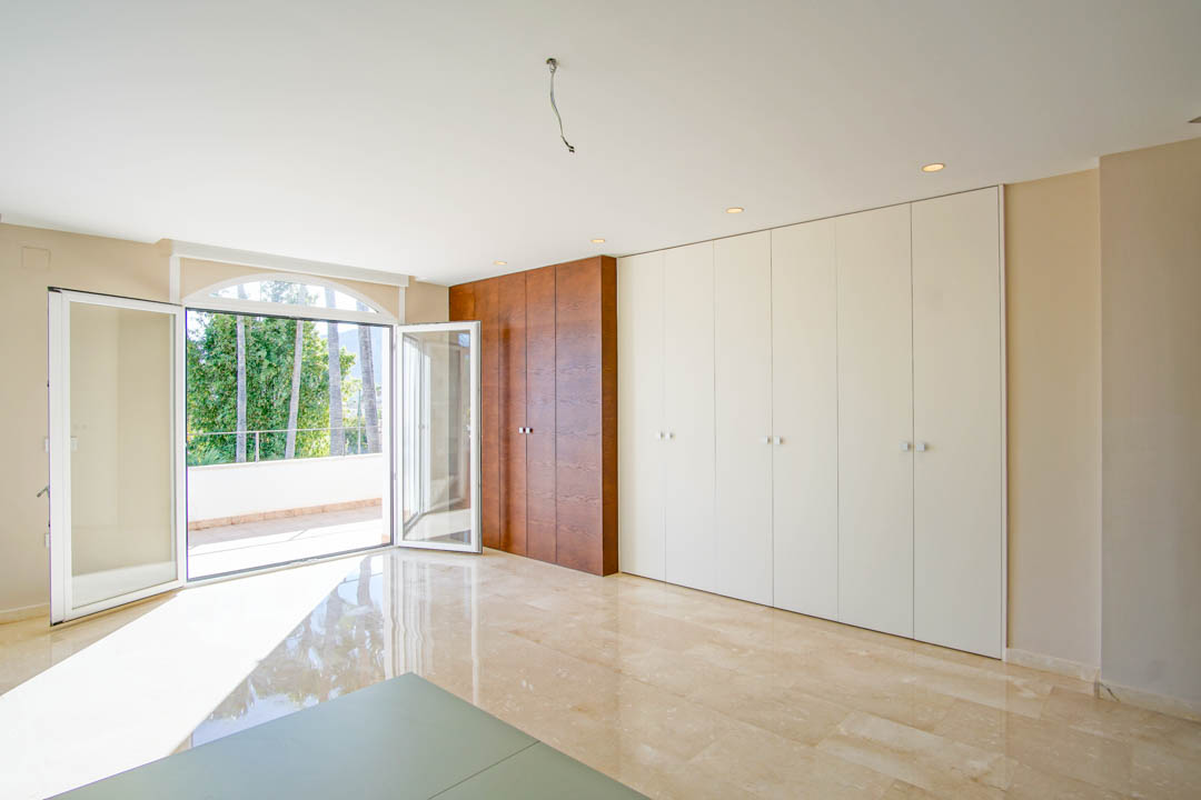 Dormitorio luminoso con armarios empotrados de diseño bicolores, suelos de mármol pulido y acceso directo a una amplia terraza privada con vistas a las palmeras.