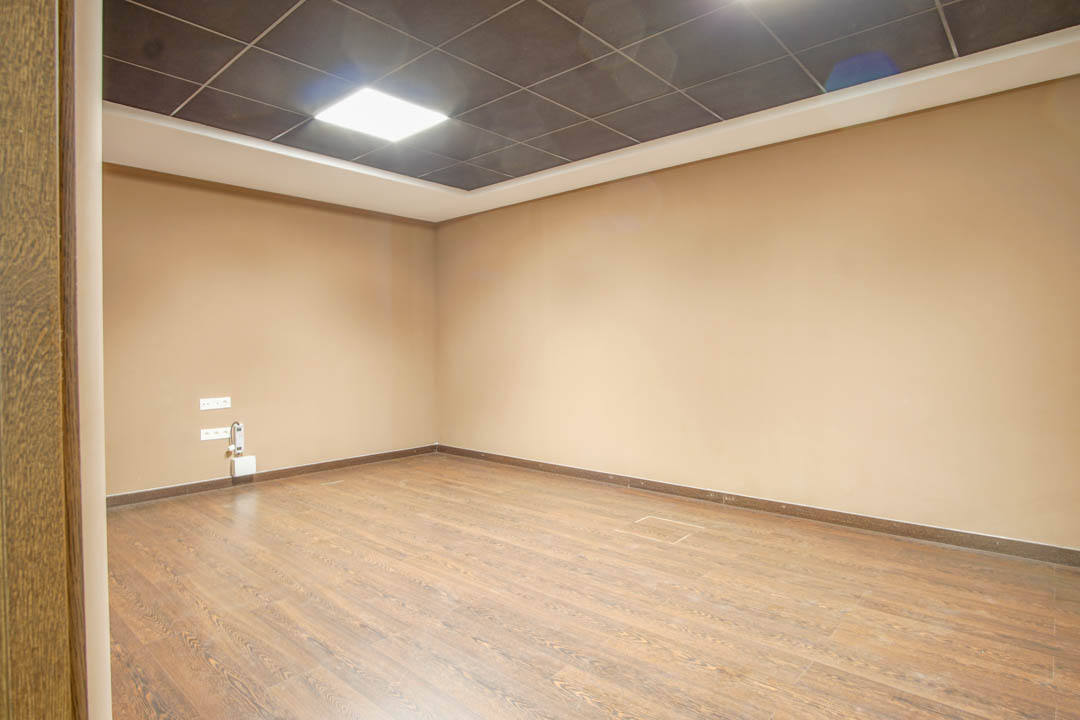 Sala polivalente en el sótano con suelos de efecto madera, paredes en tonos neutros y un techo técnico con iluminación LED integrada.