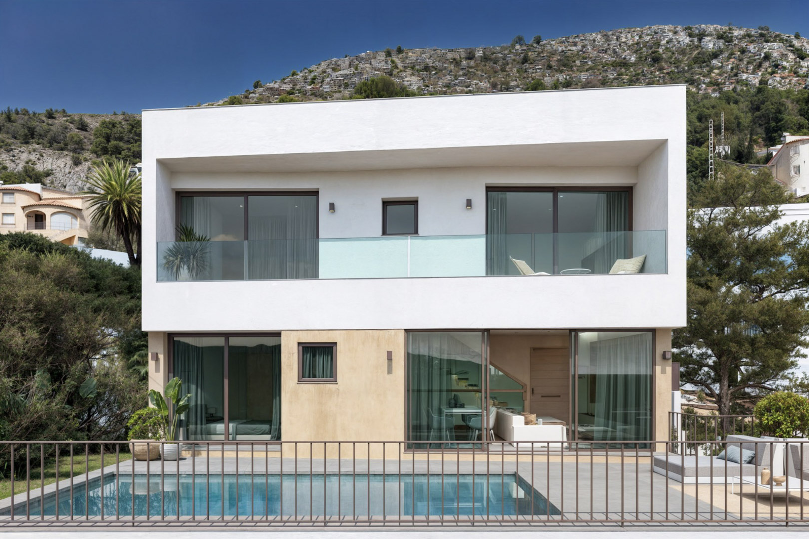 Fachada moderna de dos niveles con piscina privada, amplios ventanales de suelo a techo y terrazas con barandillas de cristal integradas en el entorno de Alcalalí.