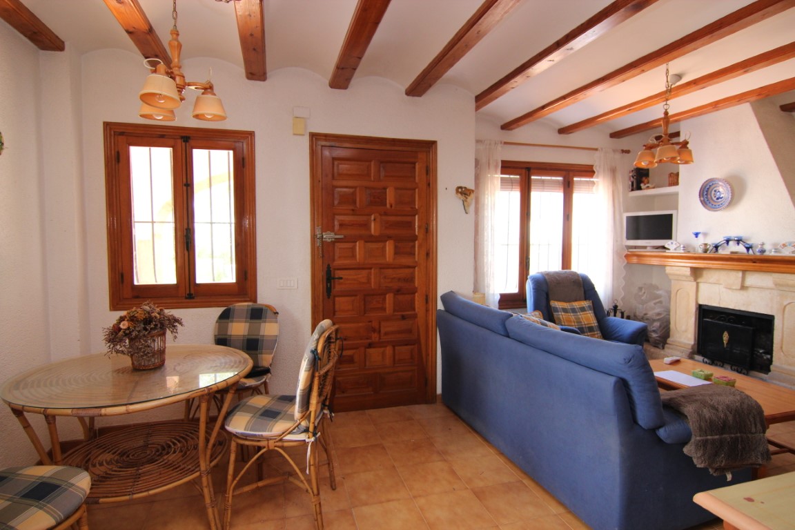 Salón comedor rústico con vigas de madera a la vista, suelos de gres, chimenea de piedra y mobiliario clásico junto a una puerta de entrada de madera maciza.