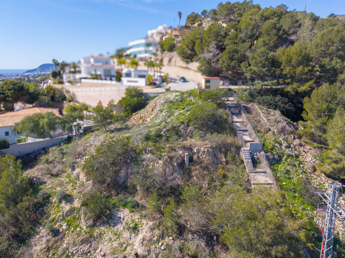 Vista elevada de la parcela escarpada en Benissa, mostrando el sendero de acceso escalonado y las vistas panorámicas hacia la costa mediterránea.