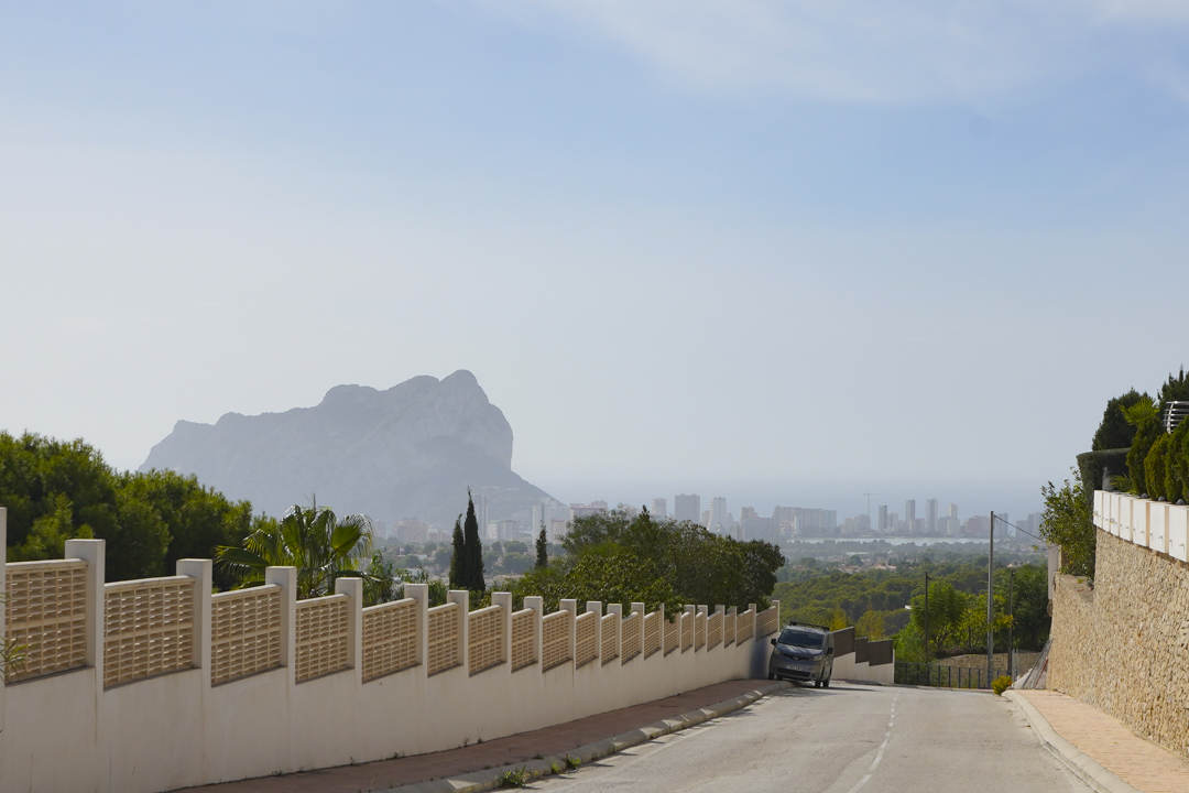 Vista panorámica desde la calle de acceso hacia el Peñón de Ifach y el skyline de Calpe, con el mar Mediterráneo de fondo bajo un cielo despejado.