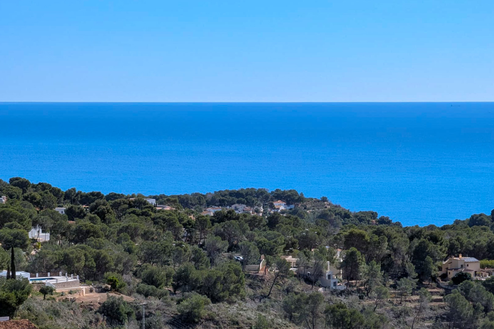 Vista panorámica desde la parcela en Tossal Los Bancales, mostrando el mar Mediterráneo y las colinas de pinos que descienden hacia la costa de Benissa.