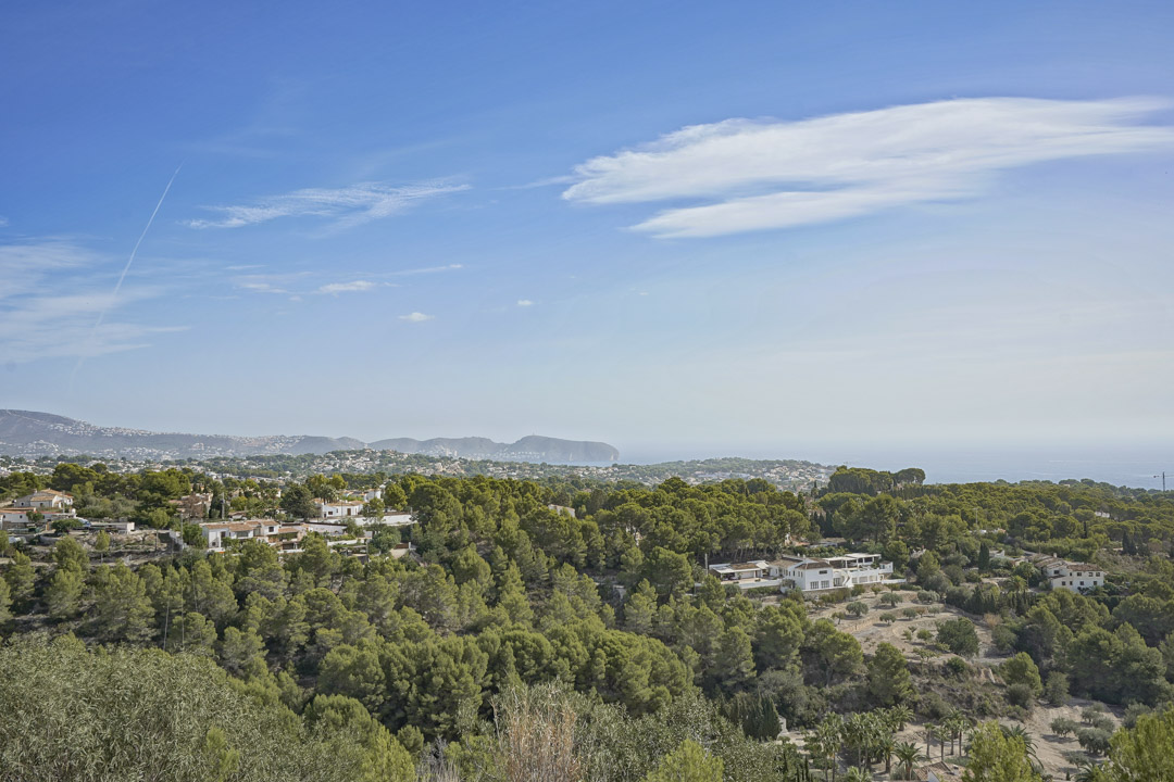 Vistas panorámicas desde la parcela hacia el mar Mediterráneo y el Cap D'or de Moraira, rodeada de frondosa vegetación de pinos y zonas residenciales.
