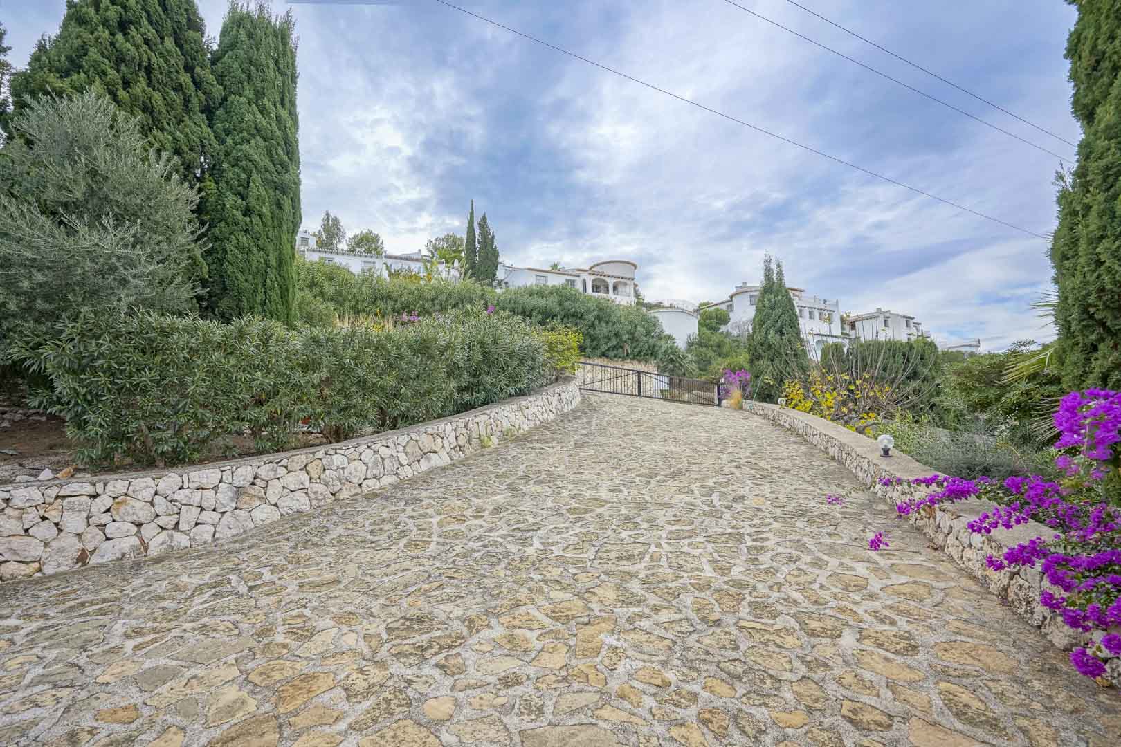 Camino de entrada de piedra natural que conduce a la villa, bordeado de jardines y vegetación.