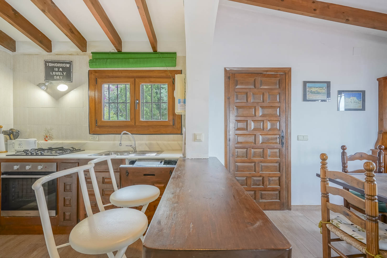 Detalle de la cocina americana con barra de madera, sillas blancas y vigas vistas en el techo.