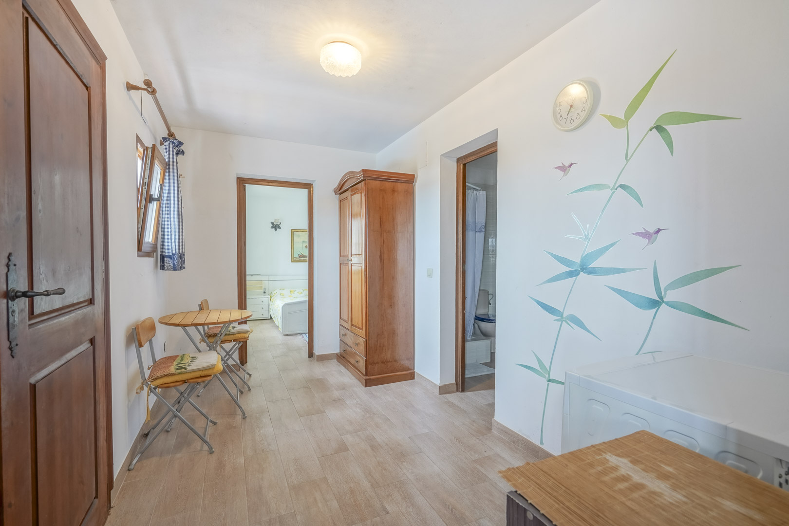 Interior luminoso con suelo de baldosas, armario de madera y decoración de pared con motivos vegetales.