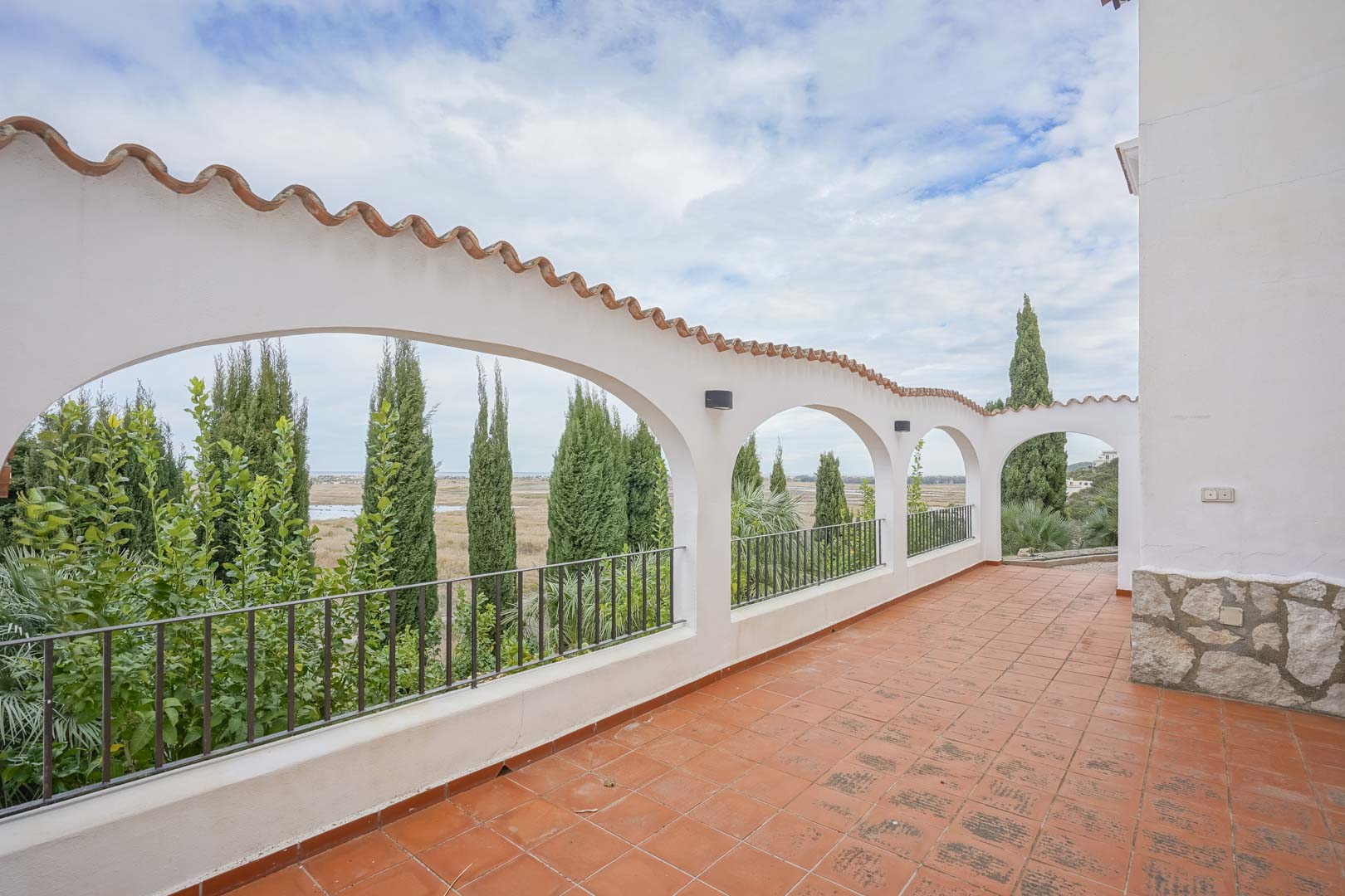 Terraza cubierta con arcos de tejas y suelo de baldosas rústicas, con vistas a la vegetación y al paisaje.