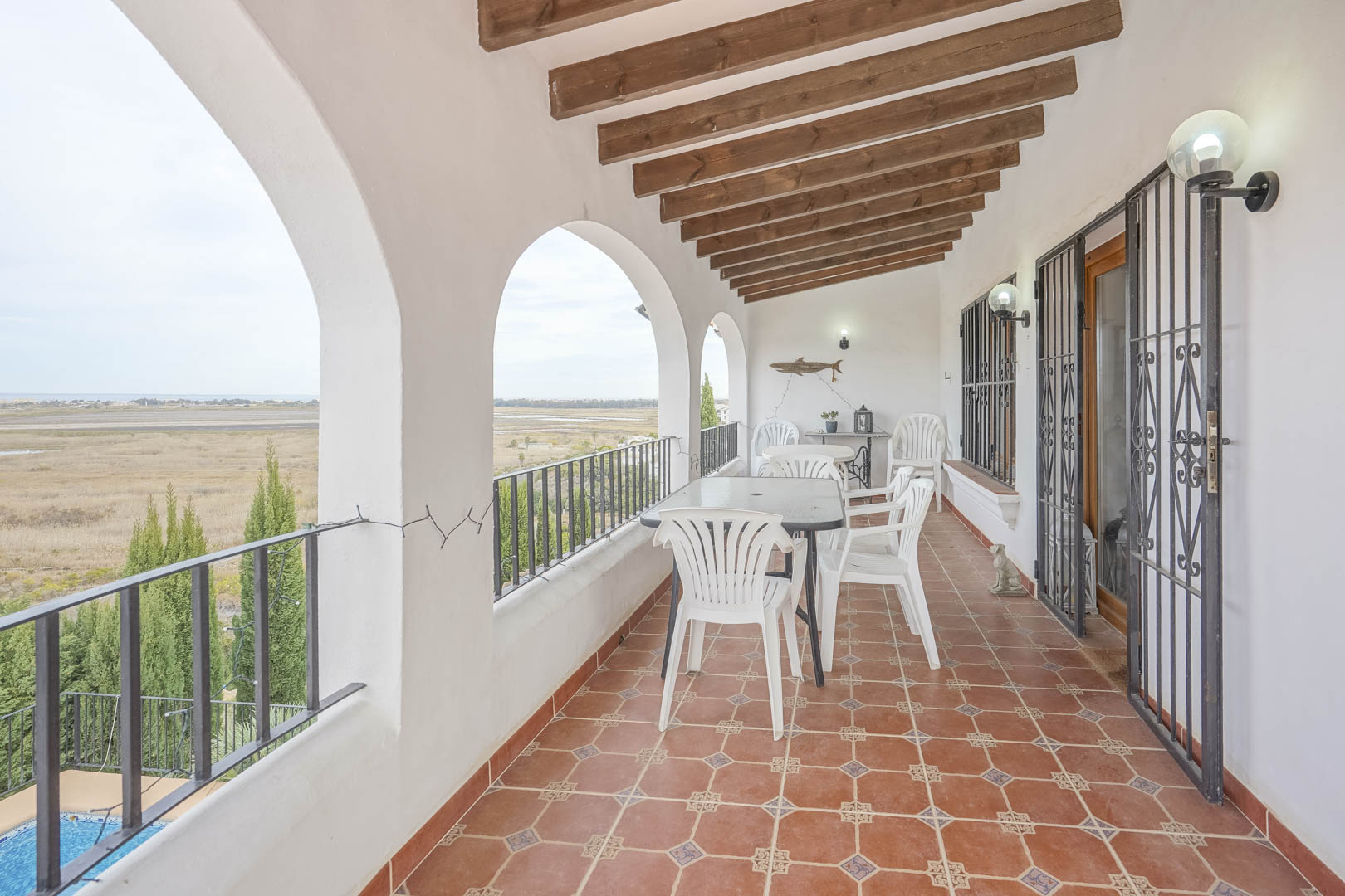 Terraza cubierta con vistas panorámicas, arcos blancos y suelo de baldosas rústicas. Mobiliario de exterior.