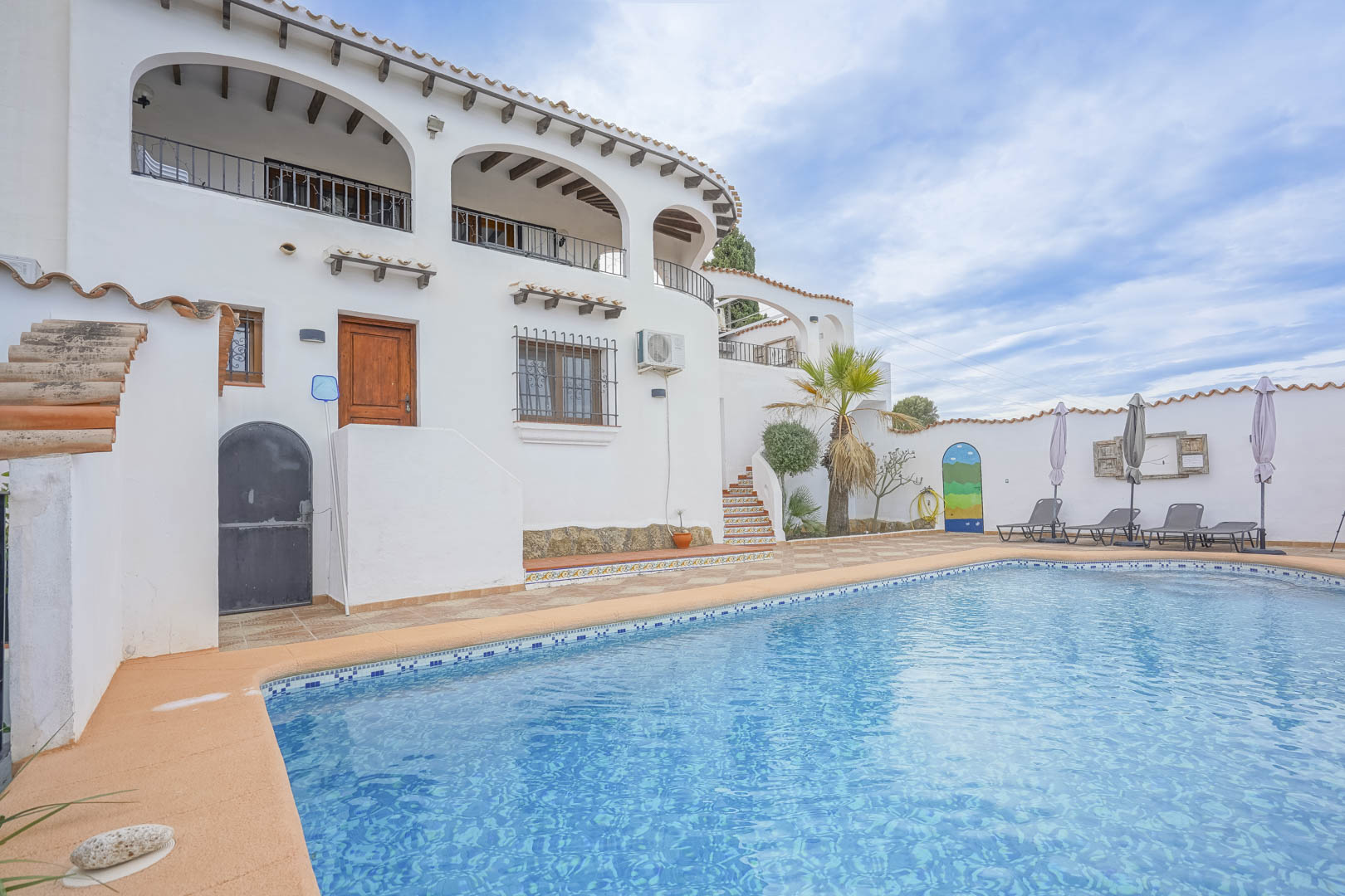 Vista de la piscina con baldosas azules y la fachada blanca de la villa de estilo castellano en Monte Pego.