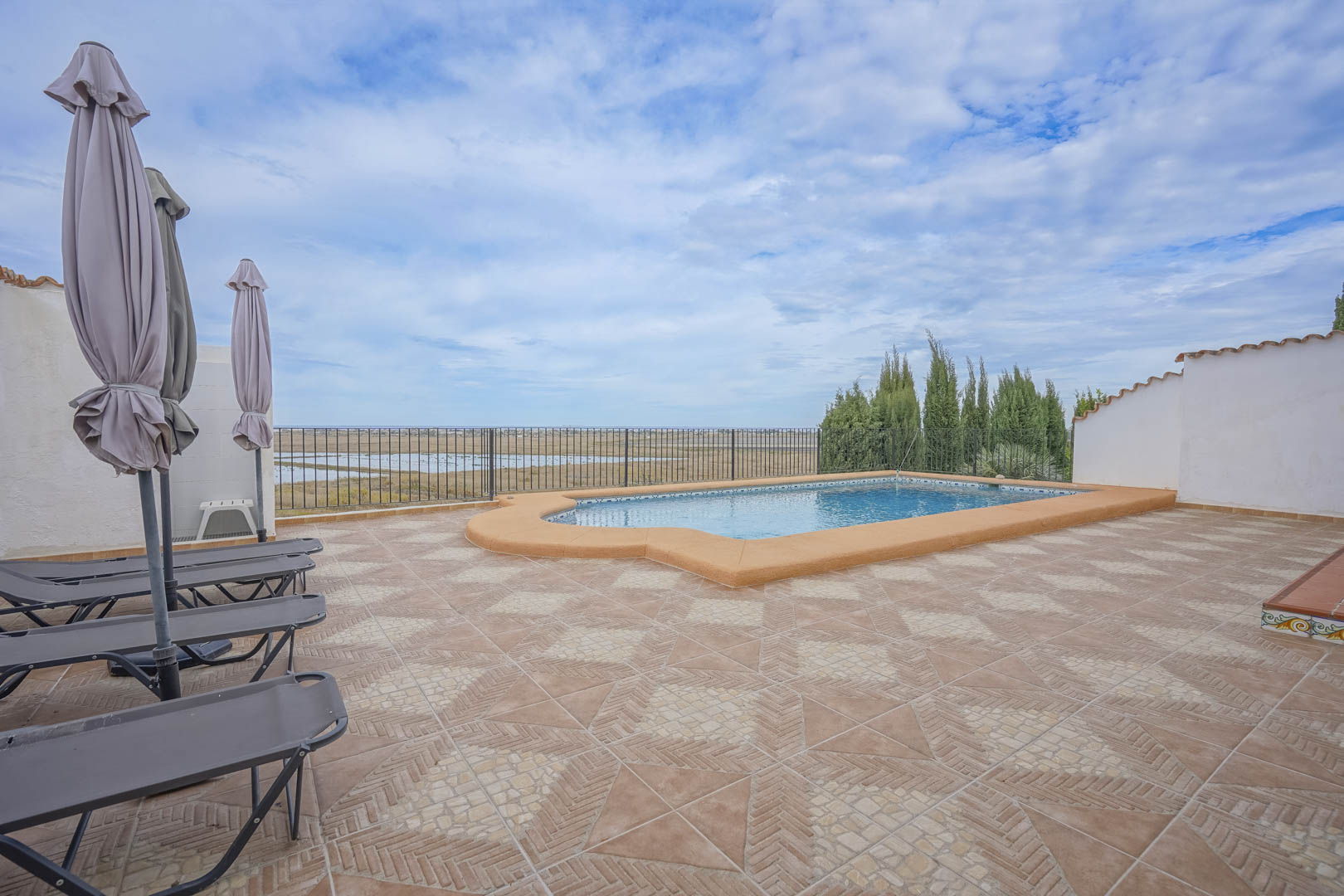 Vista de la piscina con tumbonas y sombrillas cerradas, con vistas a la reserva natural.