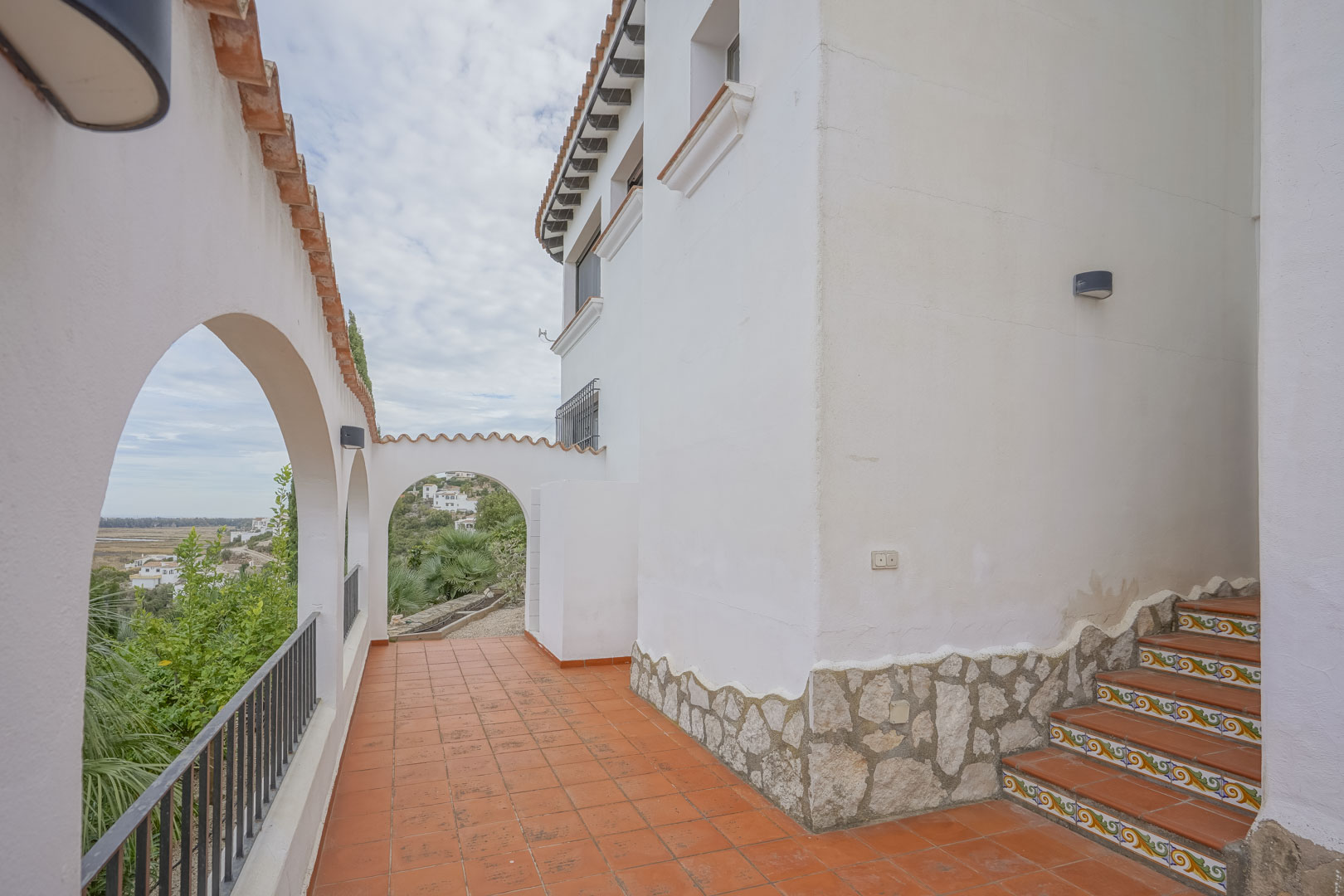 Vista exterior de la villa con arcos de estilo español, terraza de terracota y escaleras decorativas.