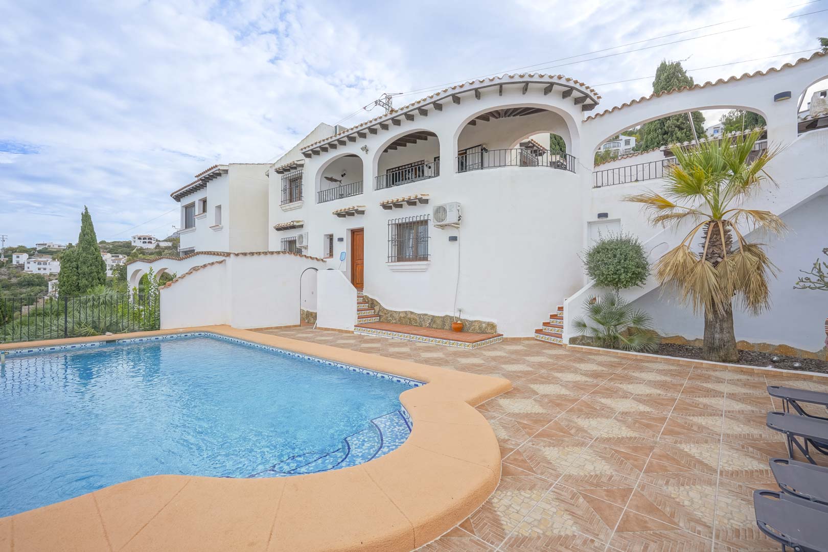 Vista exterior de la villa con piscina, terraza de baldosas y arquitectura de estilo castellano.