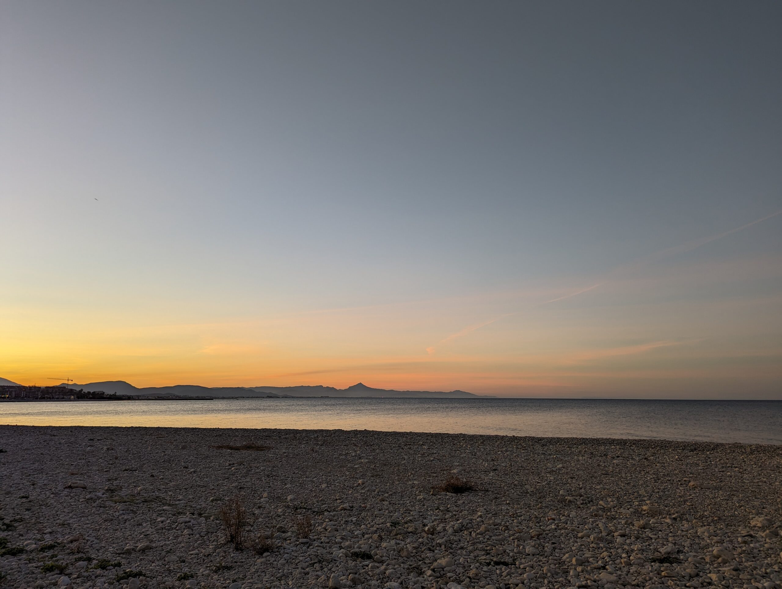 Vista de la playa de guijarros al atardecer con montañas en la distancia.