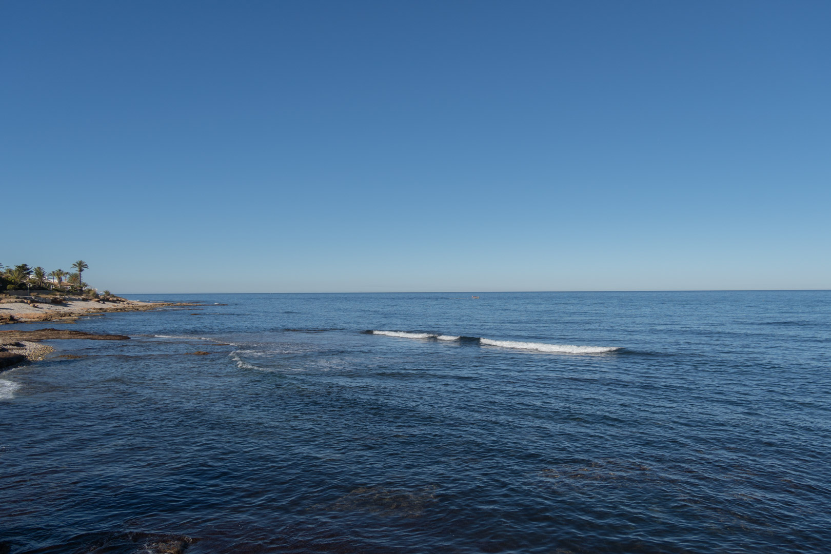 Vista del mar Mediterráneo con costa rocosa y cielo azul despejado.