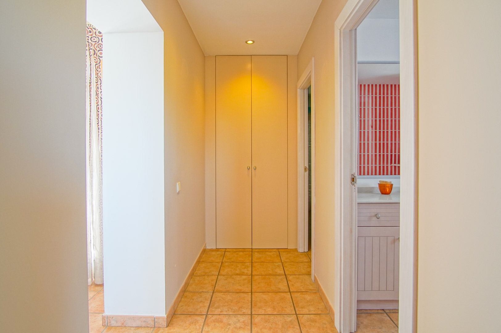Pasillo con suelos de gres cerámico que conecta las estancias, destacando un armario empotrado al fondo y acceso a un baño con azulejos decorativos de rayas rojas.
