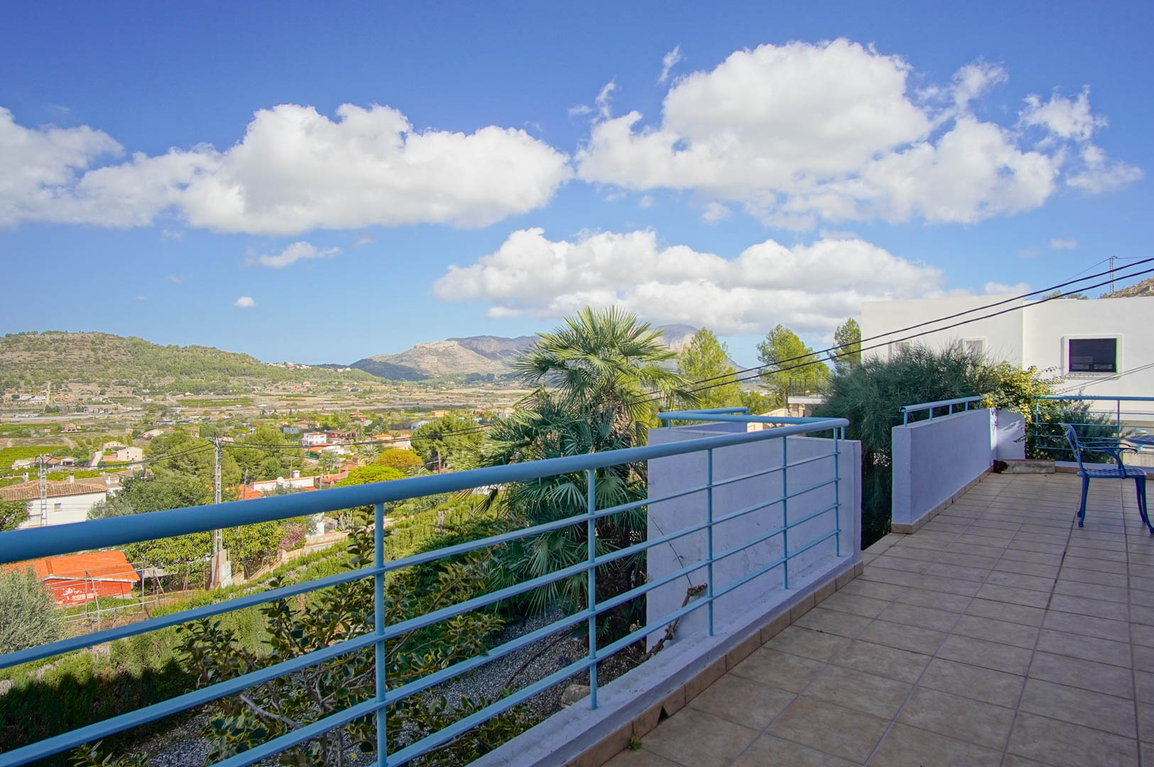 Terraza superior con suelo cerámico y barandilla azul, ofreciendo vistas panorámicas al valle de Pedreguer y las montañas circundantes bajo un cielo despejado.