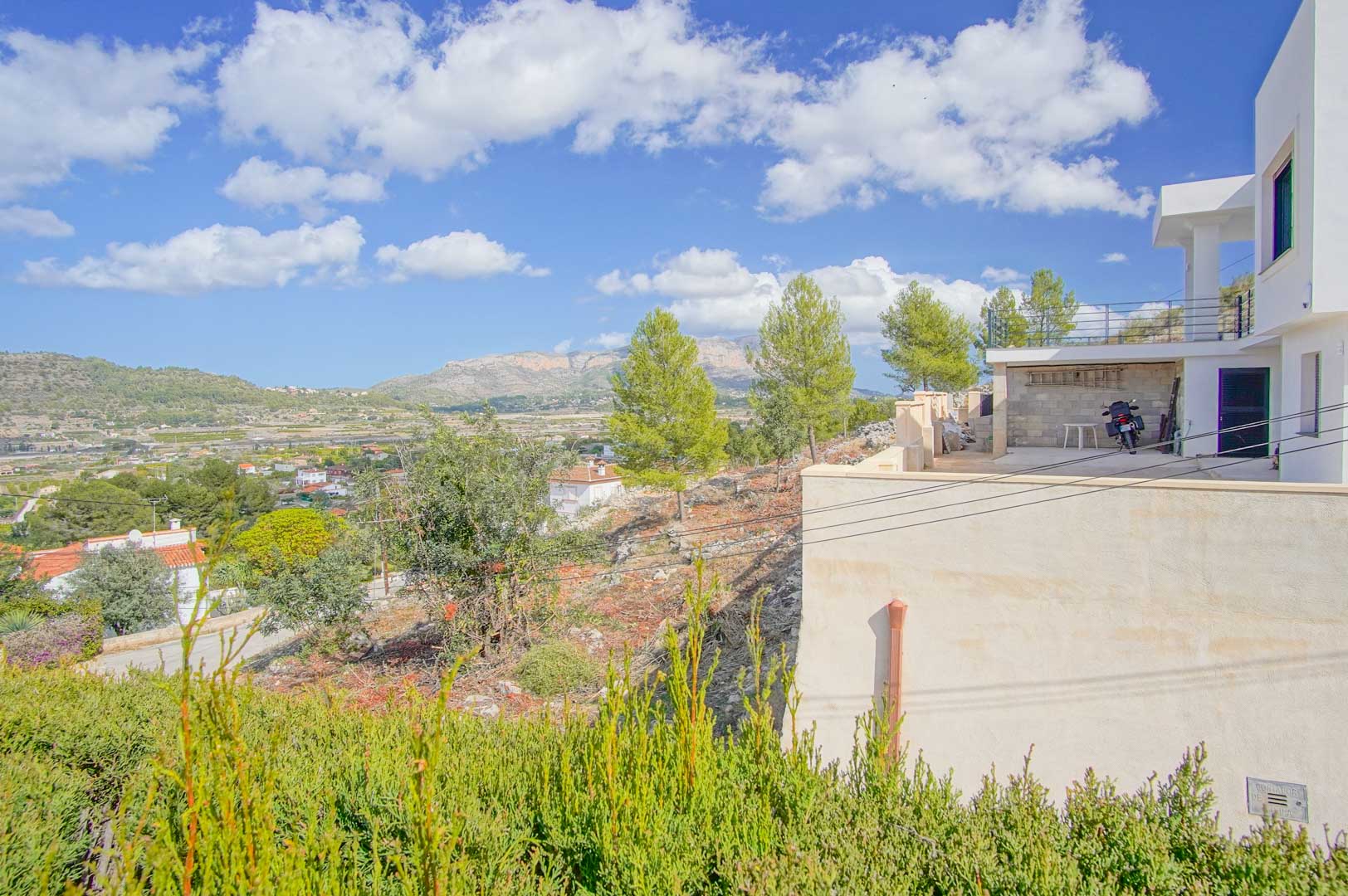 Vista exterior de la villa que muestra la zona de acceso y terraza, destacando las vistas panorámicas al valle y las montañas circundantes.