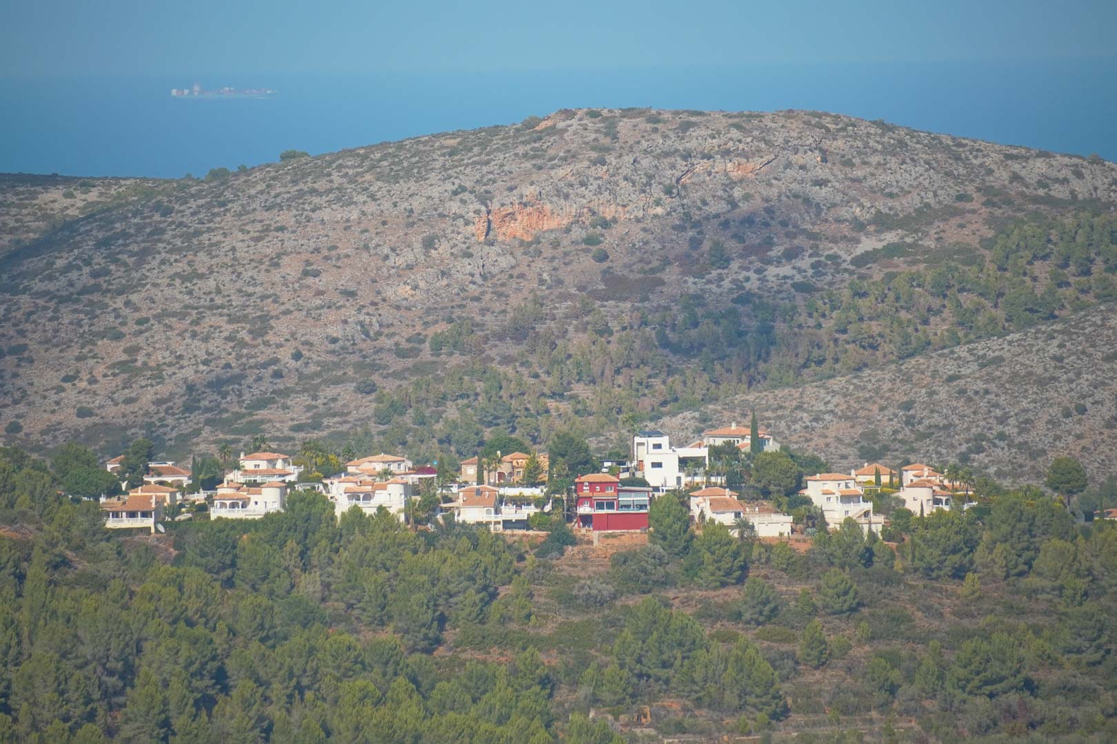 Vista panorámica desde la propiedad hacia la costa, mostrando la urbanización rodeada de pinos, la montaña y el mar Mediterráneo en el horizonte.