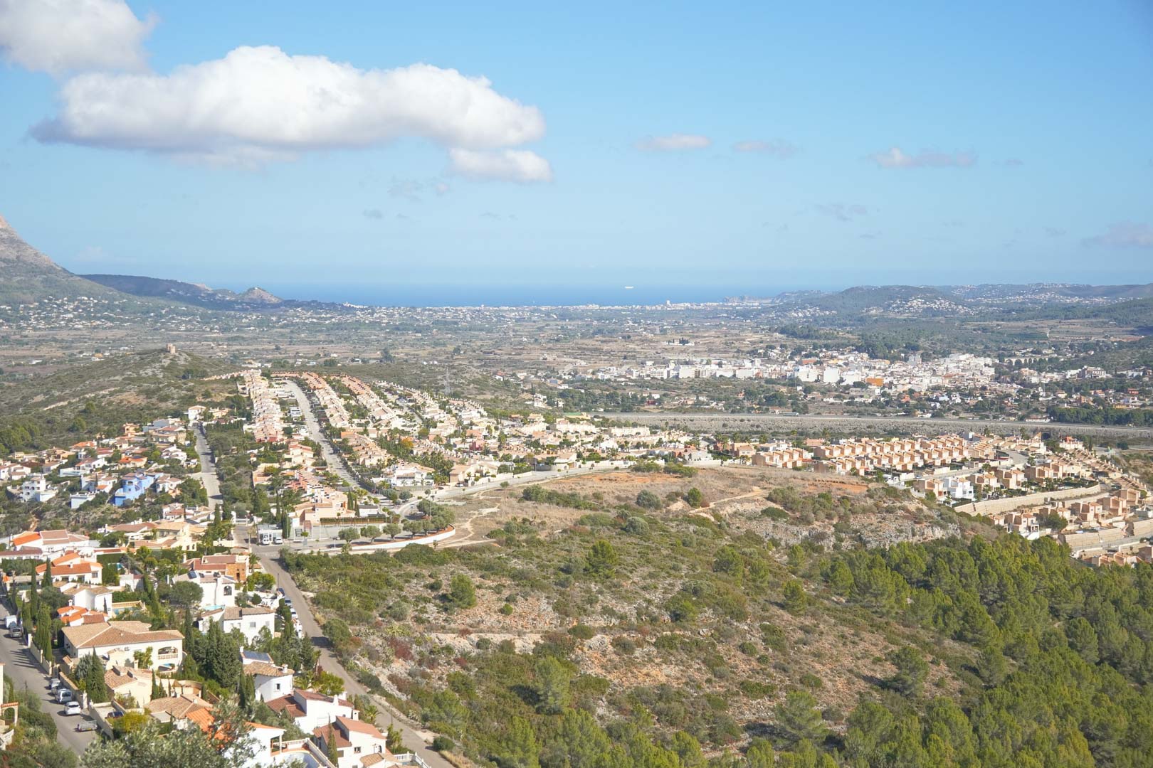 Vistas panorámicas elevadas que abarcan el valle de Pedreguer, urbanizaciones residenciales y el horizonte del mar Mediterráneo bajo un cielo despejado.