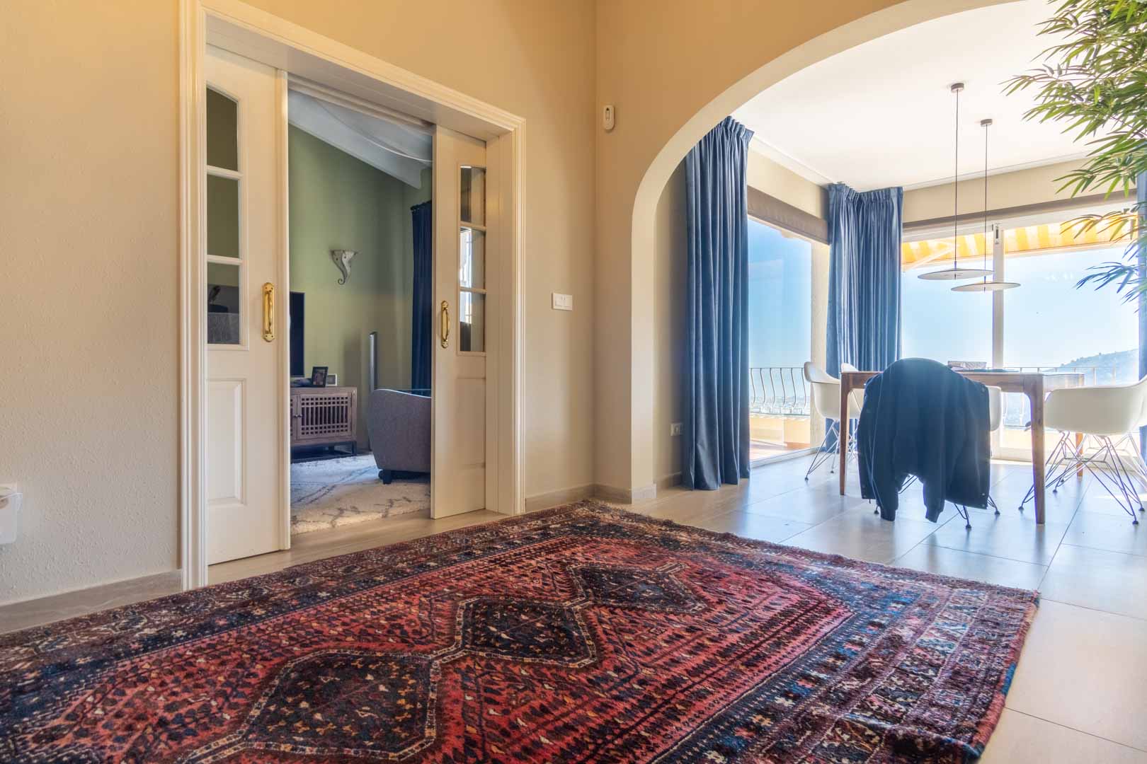 Distribuidor con alfombra de estilo oriental que conecta mediante puertas correderas acristaladas con el salón y a través de un arco con el comedor con vistas al mar.