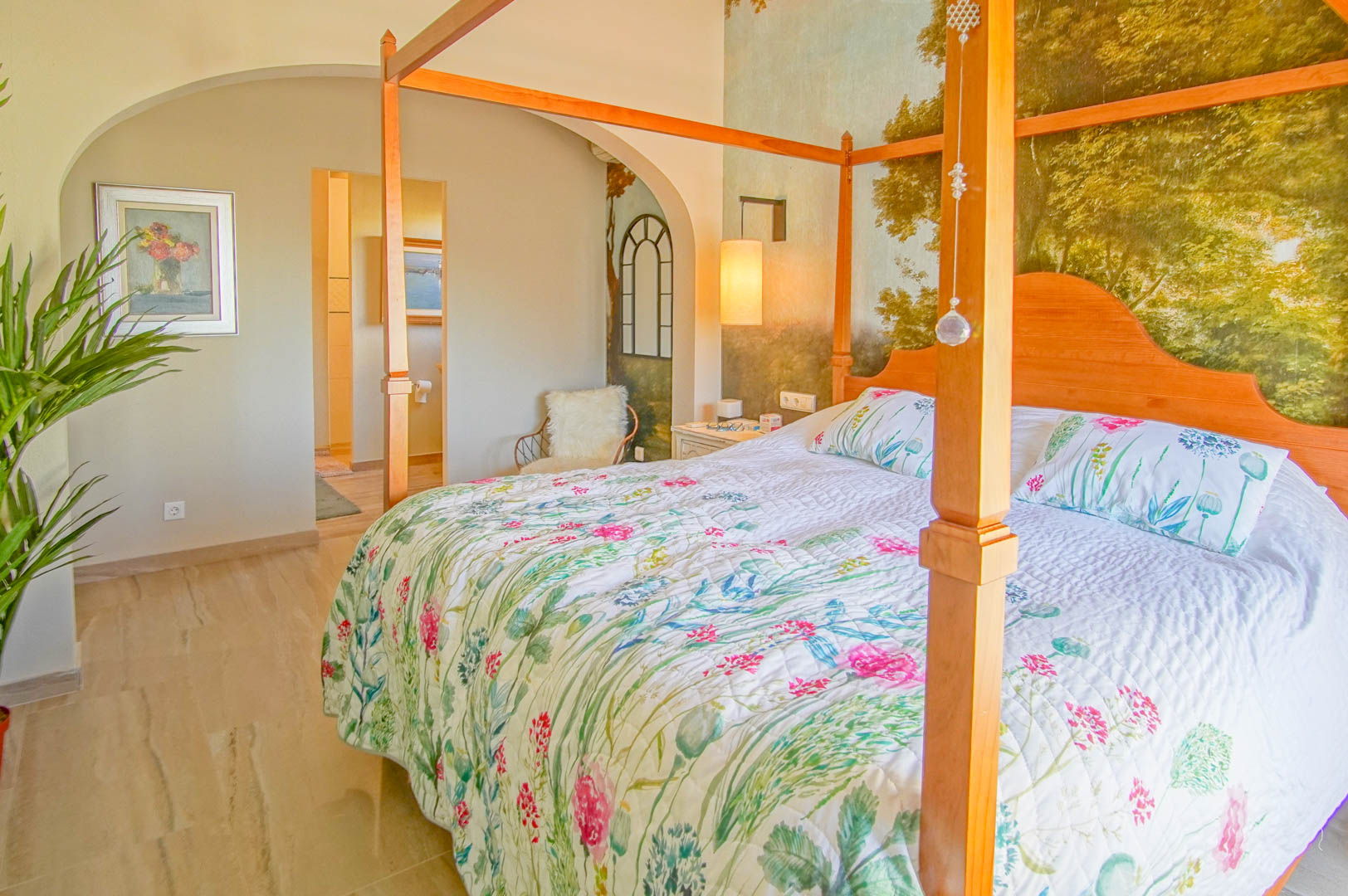 Dormitorio principal con cama de dosel en madera, mural decorativo de paisaje y suelos de mármol pulido. Incluye acceso directo al baño a través de un arco arquitectónico.