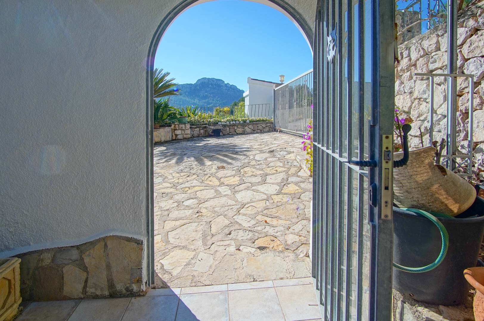 Entrada con arco de medio punto hacia una terraza de piedra irregular, destacando las vistas a la montaña y los muros de piedra seca perimetrales.